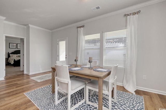 dining space with ornamental molding, baseboards, light wood finished floors, and visible vents