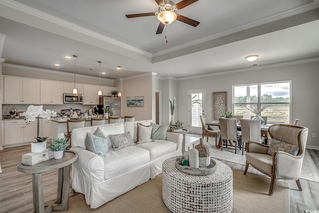 living room featuring crown molding, light hardwood / wood-style flooring, a raised ceiling, and ceiling fan