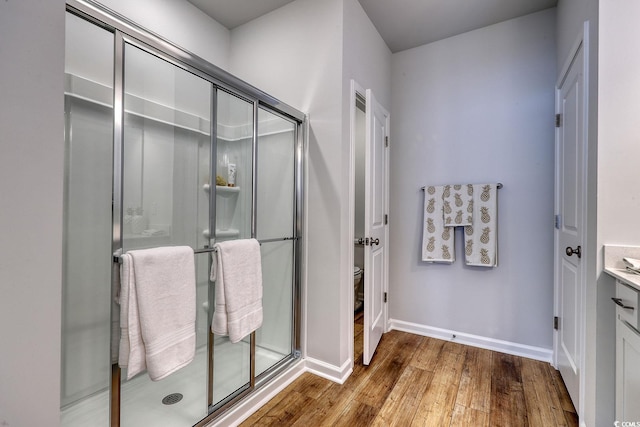 bathroom with baseboards, toilet, hardwood / wood-style flooring, a shower stall, and vanity