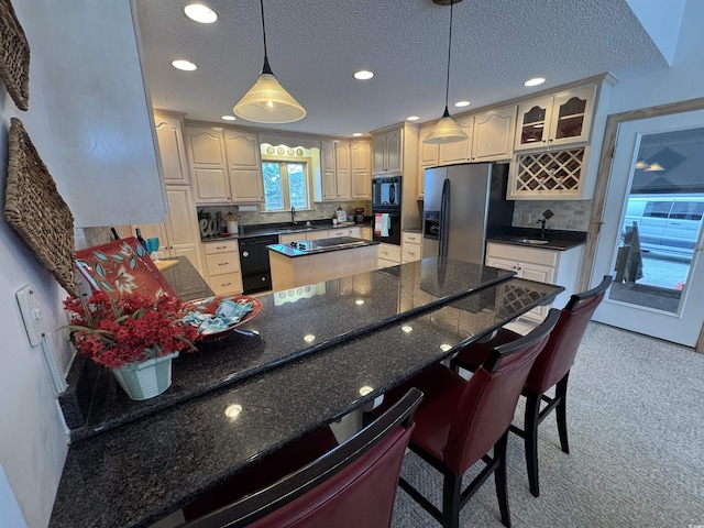 kitchen with a kitchen breakfast bar, tasteful backsplash, a textured ceiling, sink, and black appliances