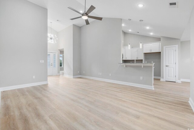 unfurnished living room with ceiling fan with notable chandelier, high vaulted ceiling, and light hardwood / wood-style flooring