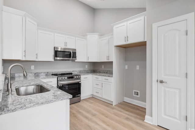 kitchen with white cabinetry, stainless steel appliances, light stone countertops, and sink