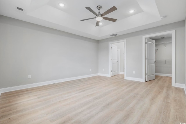 unfurnished bedroom featuring a walk in closet, a raised ceiling, a closet, ceiling fan, and light hardwood / wood-style floors