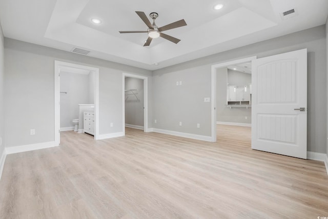 unfurnished bedroom featuring connected bathroom, a spacious closet, light wood-type flooring, a tray ceiling, and a closet