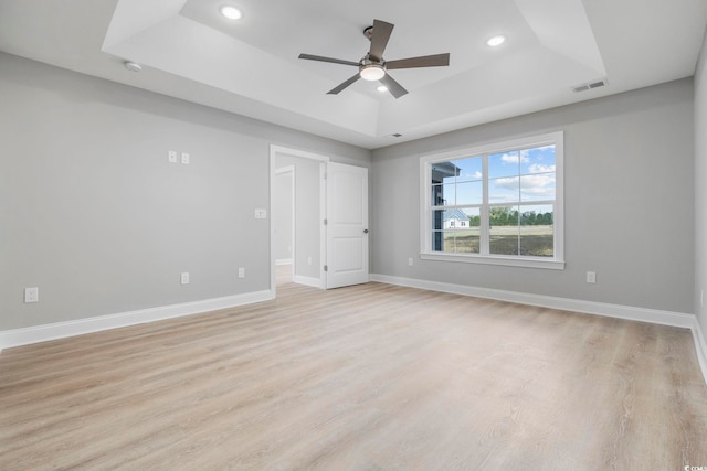 spare room with a tray ceiling, light hardwood / wood-style flooring, and ceiling fan