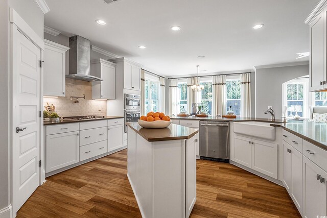 kitchen featuring appliances with stainless steel finishes, sink, wall chimney range hood, hardwood / wood-style flooring, and white cabinets