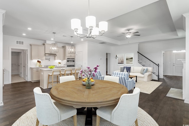 dining space featuring a tray ceiling, crown molding, ceiling fan with notable chandelier, and dark hardwood / wood-style floors