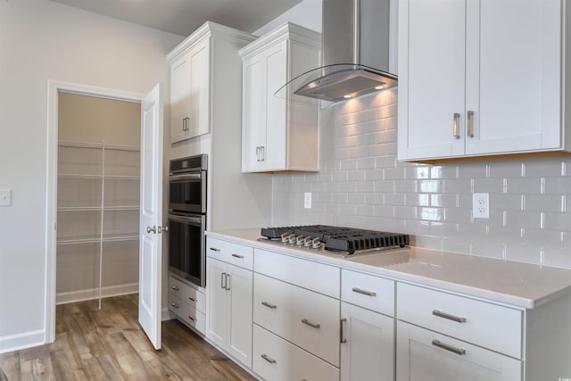 kitchen with hardwood / wood-style floors, backsplash, wall chimney exhaust hood, white cabinetry, and stainless steel appliances