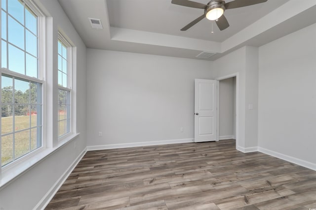 spare room featuring ceiling fan, a healthy amount of sunlight, a raised ceiling, and wood-type flooring