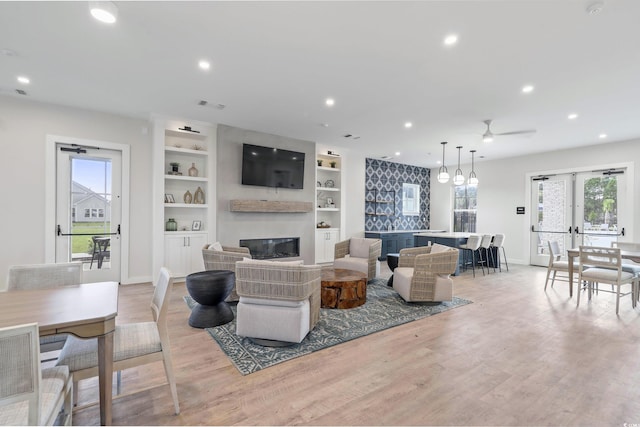 living room featuring ceiling fan, french doors, built in shelves, and light hardwood / wood-style flooring