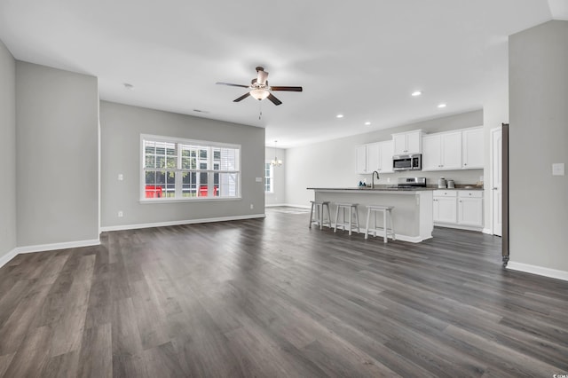 unfurnished living room with dark wood-style floors, recessed lighting, ceiling fan with notable chandelier, and baseboards