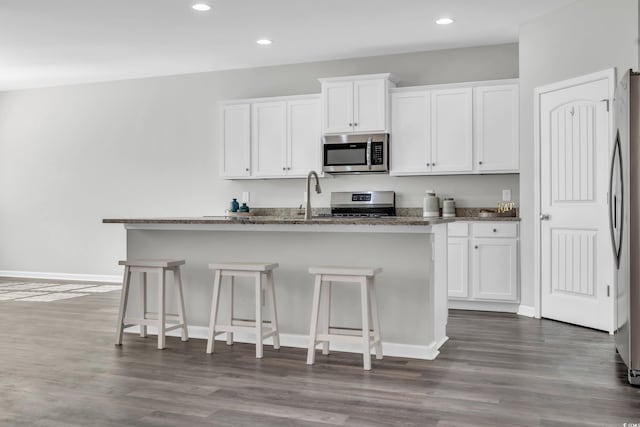 kitchen featuring stainless steel appliances, a breakfast bar area, a kitchen island with sink, and white cabinets