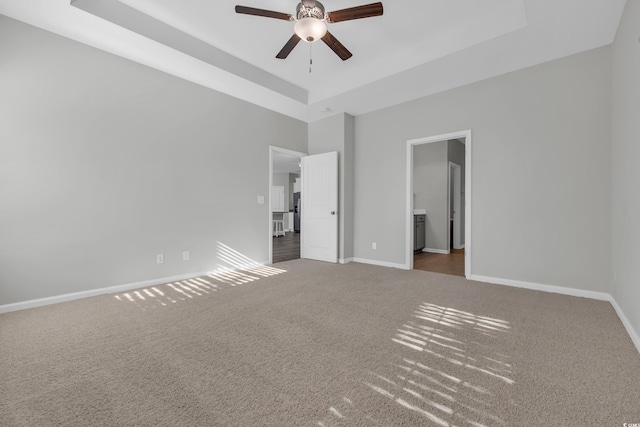 unfurnished bedroom featuring carpet, baseboards, a raised ceiling, and connected bathroom