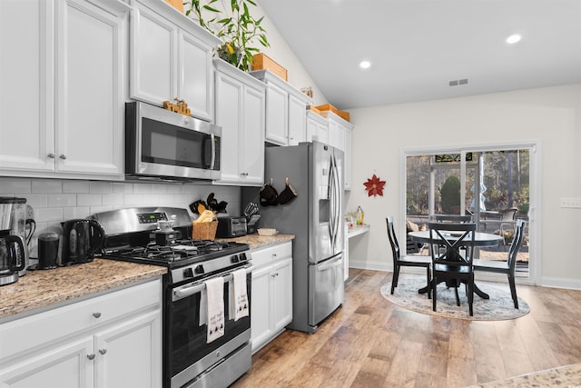 kitchen featuring white cabinetry, backsplash, light stone counters, light hardwood / wood-style floors, and stainless steel appliances