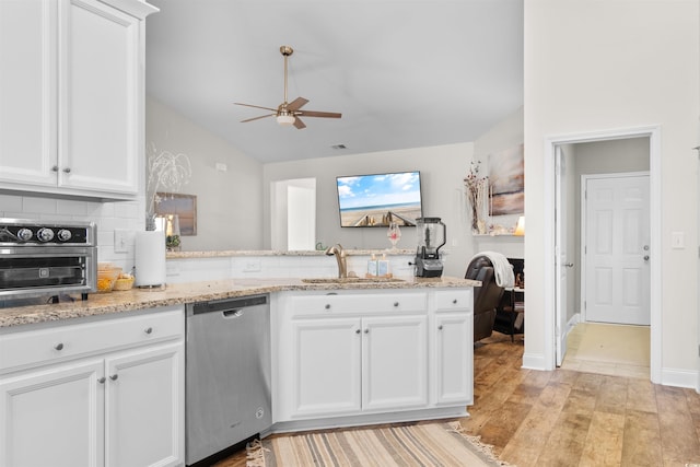 kitchen featuring sink, light stone countertops, white cabinets, vaulted ceiling, and stainless steel dishwasher