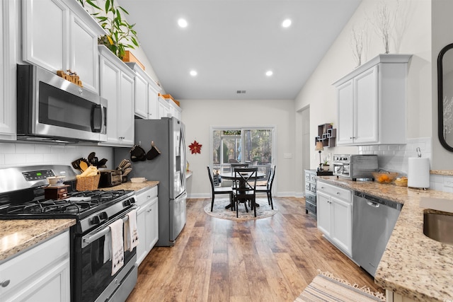 kitchen featuring light wood-type flooring, stainless steel appliances, light stone countertops, decorative backsplash, and white cabinets