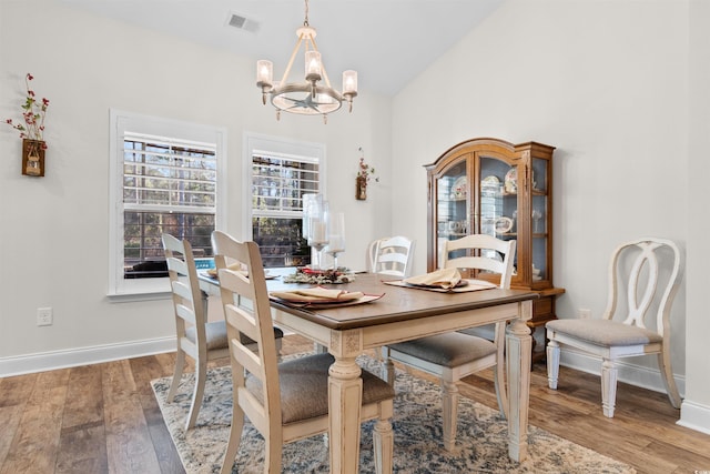 dining area with a notable chandelier, vaulted ceiling, and wood-type flooring