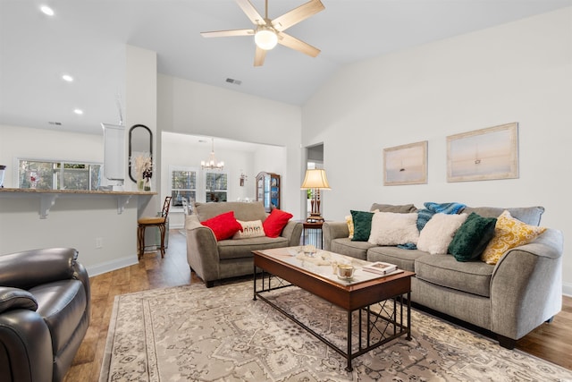 living room with vaulted ceiling, ceiling fan with notable chandelier, and light hardwood / wood-style floors