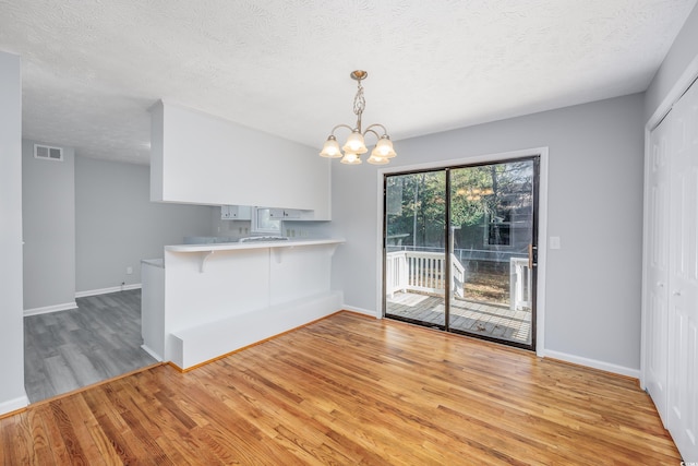 kitchen with hanging light fixtures, a kitchen breakfast bar, a notable chandelier, kitchen peninsula, and light wood-type flooring