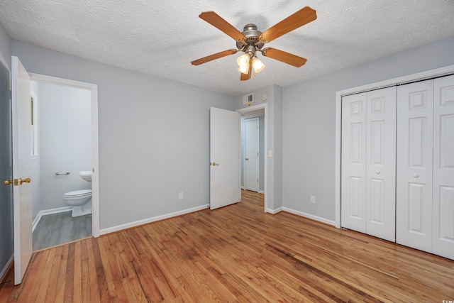 unfurnished bedroom with ensuite bathroom, a textured ceiling, ceiling fan, light hardwood / wood-style flooring, and a closet