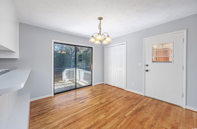 unfurnished dining area with a notable chandelier, light hardwood / wood-style floors, and a textured ceiling