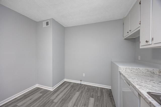 interior space with light wood-type flooring, a textured ceiling, white dishwasher, and white cabinetry