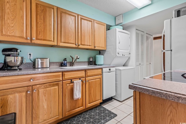 kitchen featuring sink, stacked washer / dryer, a textured ceiling, white appliances, and light tile patterned floors