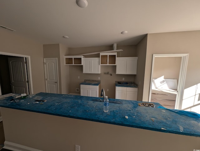 kitchen with a kitchen island with sink, white cabinetry, sink, and dark stone counters