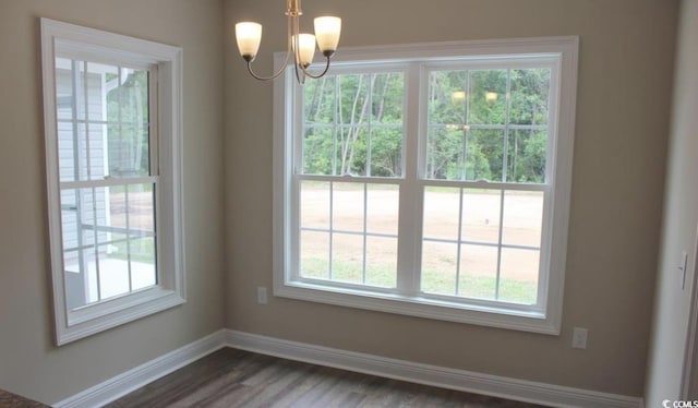 unfurnished dining area featuring an inviting chandelier, a wealth of natural light, and dark wood-type flooring