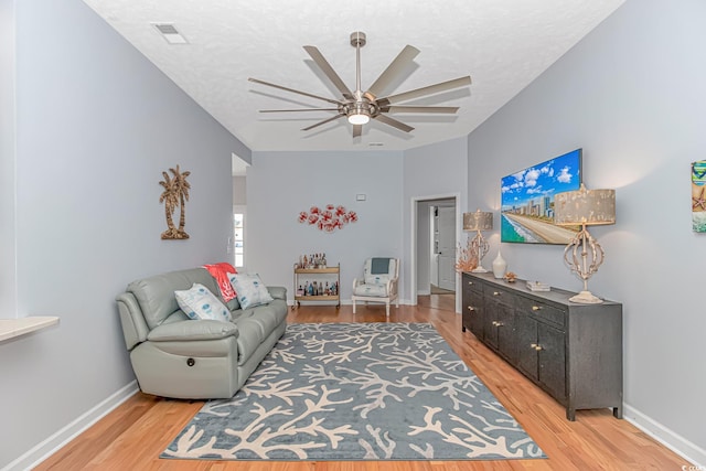 living room featuring ceiling fan, light wood-type flooring, and a textured ceiling