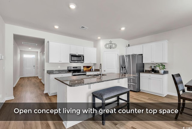 kitchen featuring appliances with stainless steel finishes, sink, dark stone countertops, white cabinetry, and an island with sink