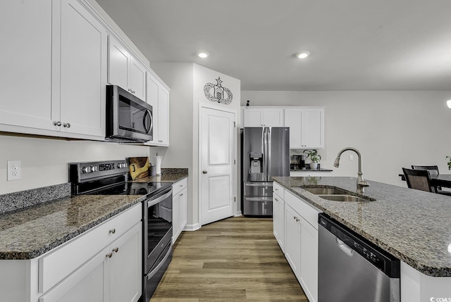 kitchen with a kitchen island with sink, dark stone counters, white cabinets, sink, and stainless steel appliances