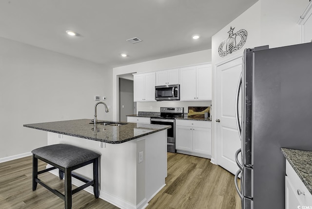 kitchen with appliances with stainless steel finishes, sink, dark stone countertops, white cabinetry, and an island with sink