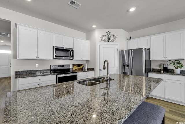 kitchen with appliances with stainless steel finishes, sink, a center island with sink, dark stone countertops, and white cabinets