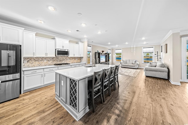 kitchen with white cabinets, a center island with sink, sink, a kitchen bar, and stainless steel appliances