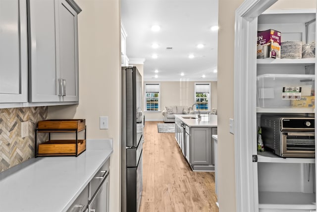 kitchen with tasteful backsplash, gray cabinets, light hardwood / wood-style flooring, and stainless steel refrigerator