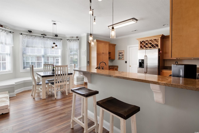 kitchen featuring a breakfast bar area, crown molding, pendant lighting, and stainless steel refrigerator with ice dispenser