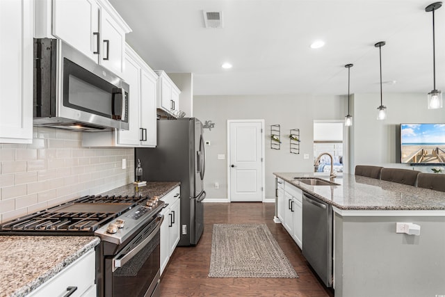 kitchen with a center island with sink, sink, hanging light fixtures, white cabinetry, and stainless steel appliances