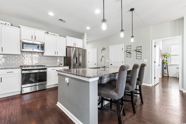 kitchen with white cabinets, pendant lighting, stainless steel appliances, and an island with sink