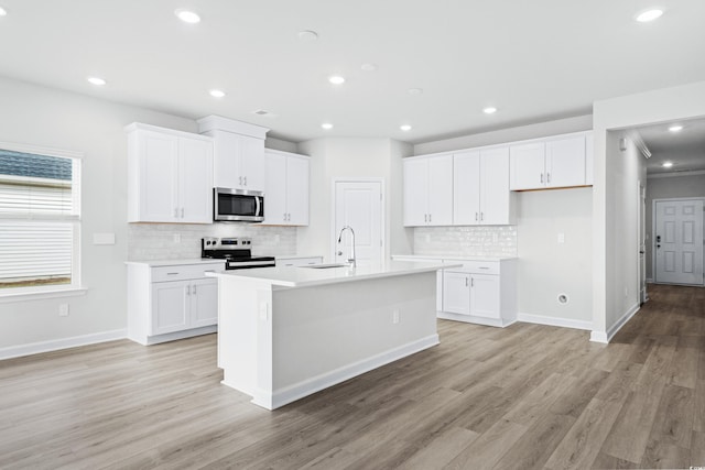 kitchen with appliances with stainless steel finishes, a center island with sink, white cabinets, and light hardwood / wood-style flooring