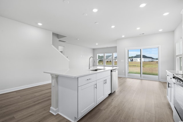 kitchen featuring electric stove, sink, dishwasher, white cabinetry, and a center island with sink