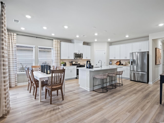 kitchen with stainless steel appliances, a breakfast bar, an island with sink, and white cabinets