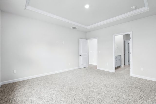 unfurnished bedroom with a raised ceiling, ornamental molding, connected bathroom, and light colored carpet