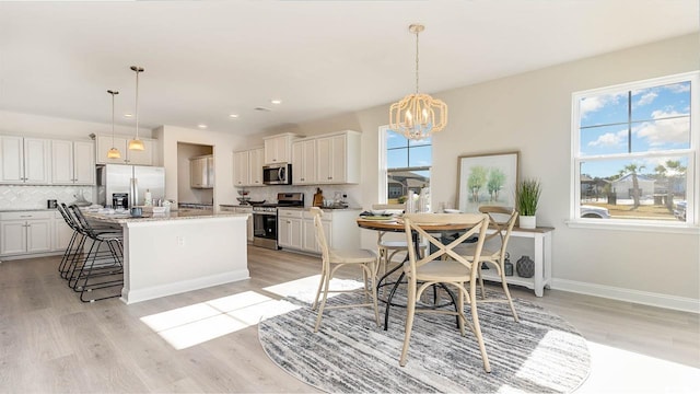 kitchen featuring pendant lighting, white cabinets, stainless steel appliances, tasteful backsplash, and a center island with sink