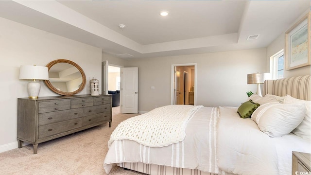 bedroom featuring light carpet, a tray ceiling, and ensuite bathroom