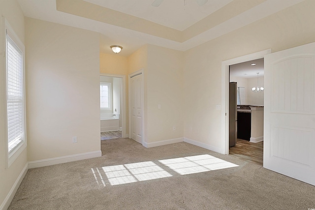 carpeted spare room featuring ceiling fan with notable chandelier and a raised ceiling