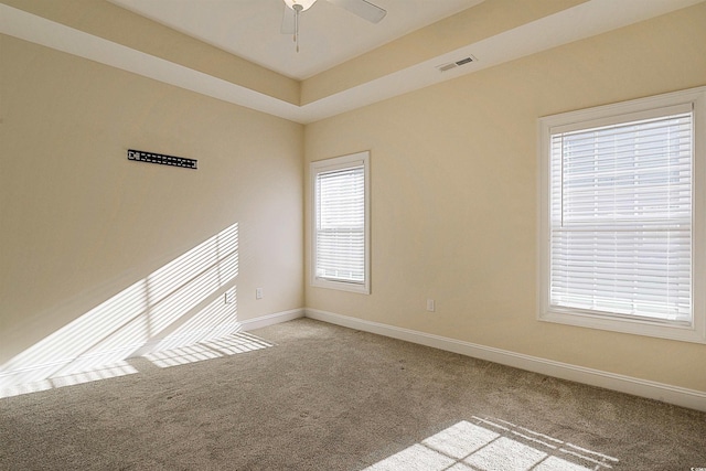 unfurnished room with ceiling fan, a raised ceiling, and light carpet