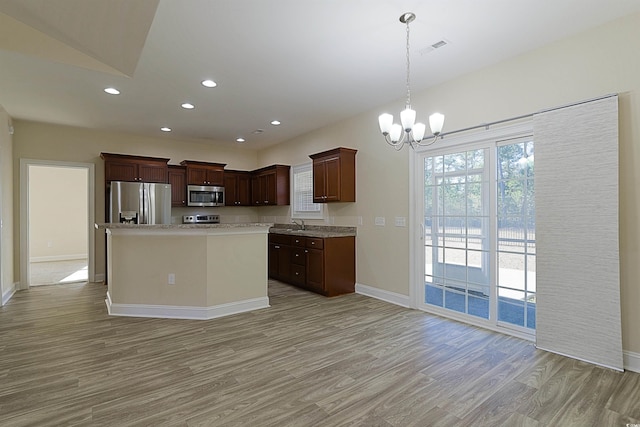 kitchen featuring dark brown cabinetry, appliances with stainless steel finishes, decorative light fixtures, a kitchen island, and light wood-type flooring