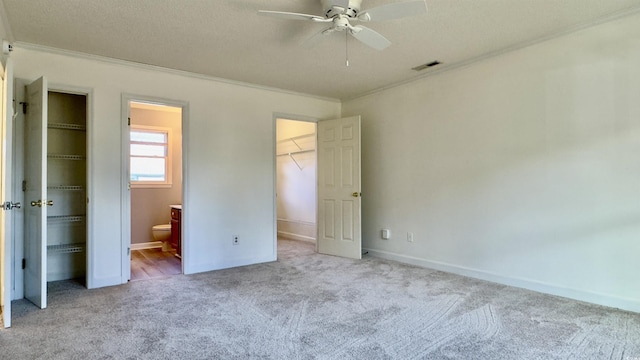 unfurnished bedroom featuring a walk in closet, ornamental molding, a closet, and light carpet