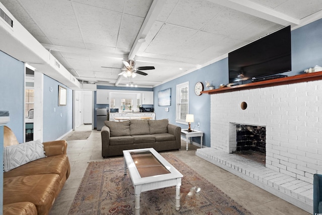 living room with ceiling fan, crown molding, light tile patterned floors, beamed ceiling, and a fireplace